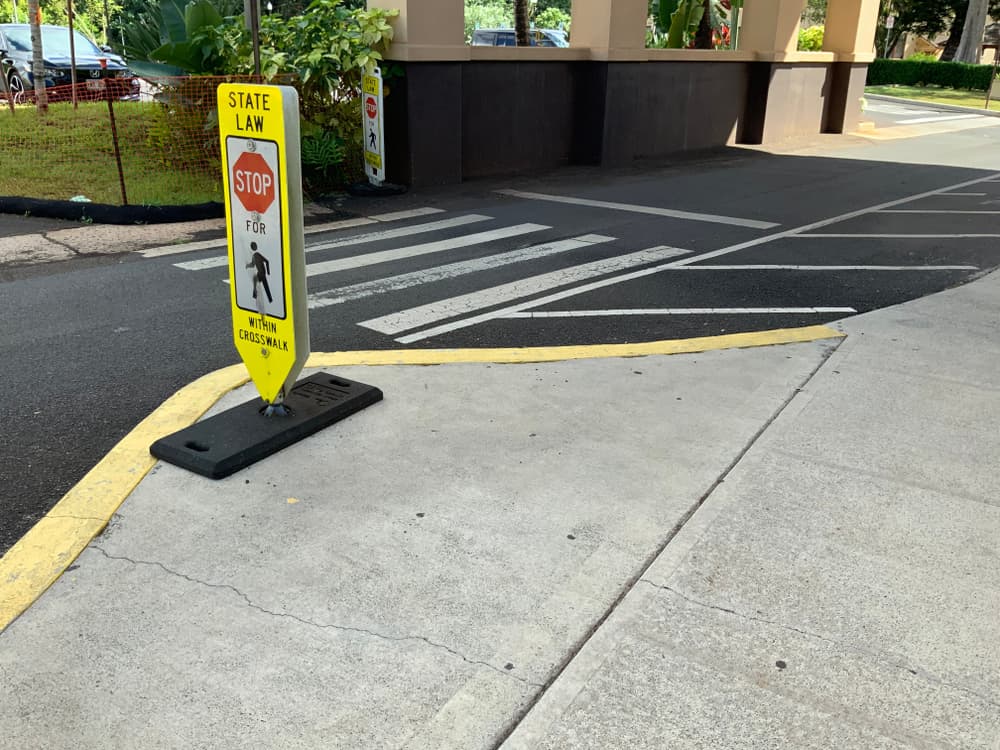 Crosswalk with a "State Law: Stop for Pedestrians within Crosswalk" sign on a sidewalk.