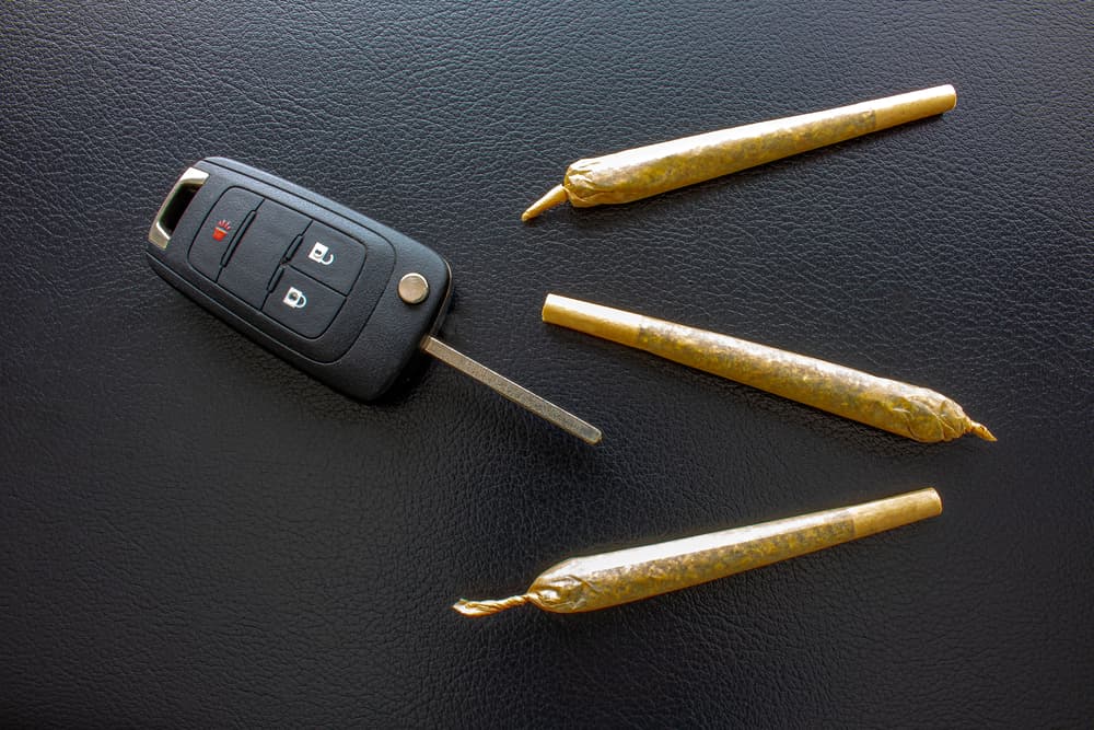 A car key fob placed next to three rolled marijuana joints on a black surface.