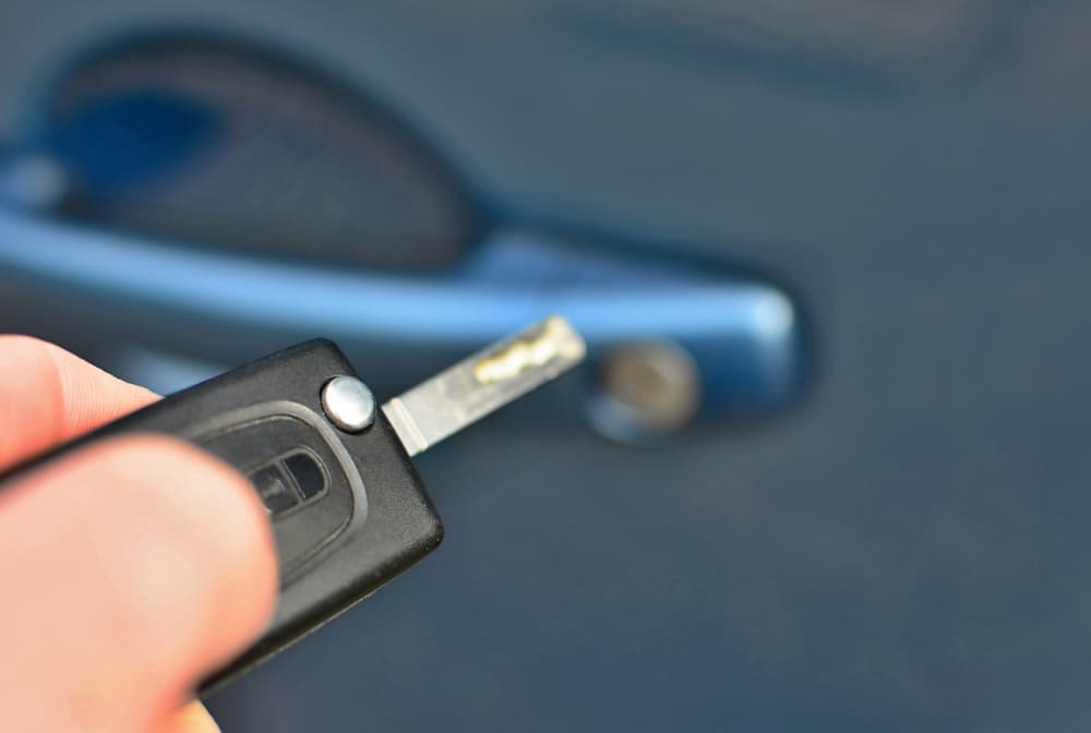 A person holding a car key near a blue car door's lock and handle.