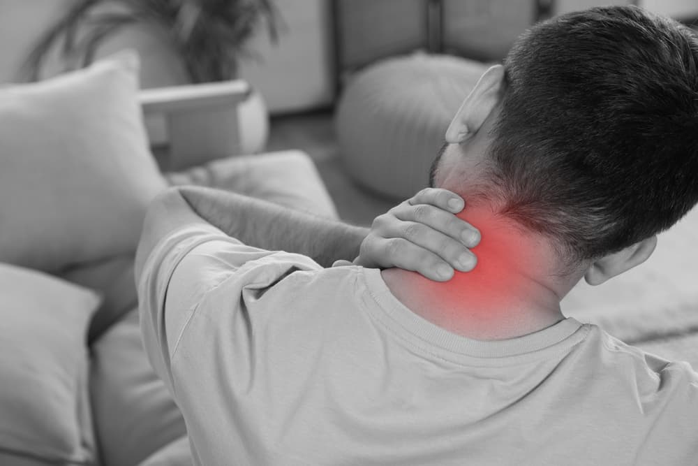 A man holding his neck in pain, highlighting neck discomfort with a red inflamed area.