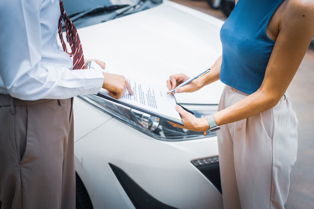 Two people standing in front of a car, reviewing and signing a document on a clipboard.