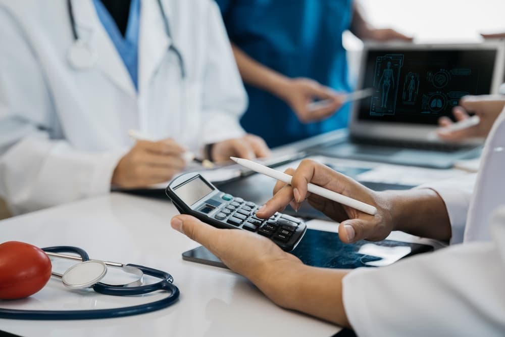 Doctors in white coats discussing medical documents while one uses a calculator and a pen.