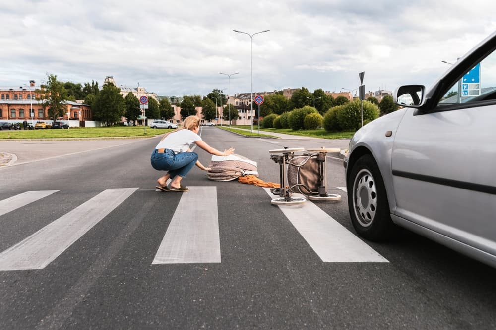 A woman helps a fallen person in a crosswalk after a car accident nearby.