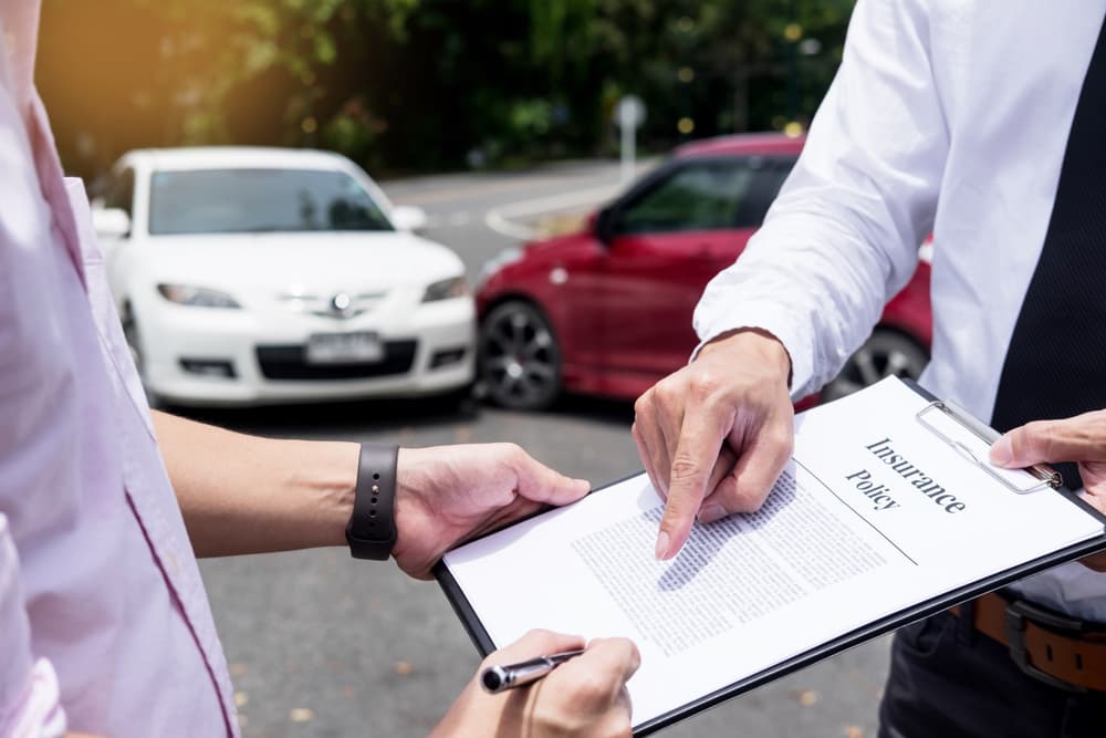 Two people examining an insurance policy document with cars involved in an accident in the background.