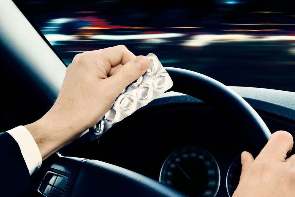 A person driving a car while holding a blister pack of pills in their hand.