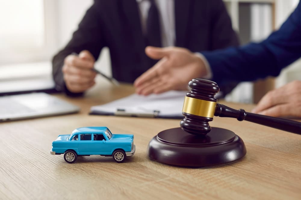 Two people discussing legal documents at a desk with a gavel and a toy car.