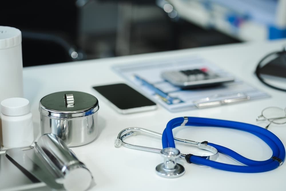 A stethoscope, medical supplies, and a smartphone on a doctor's desk with documents nearby.