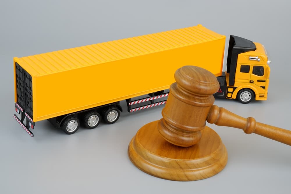 Wooden gavel and yellow cargo truck on grey background.