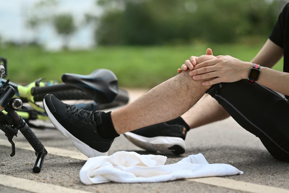 Man cyclist with injured knee sitting near bicycle outdoors