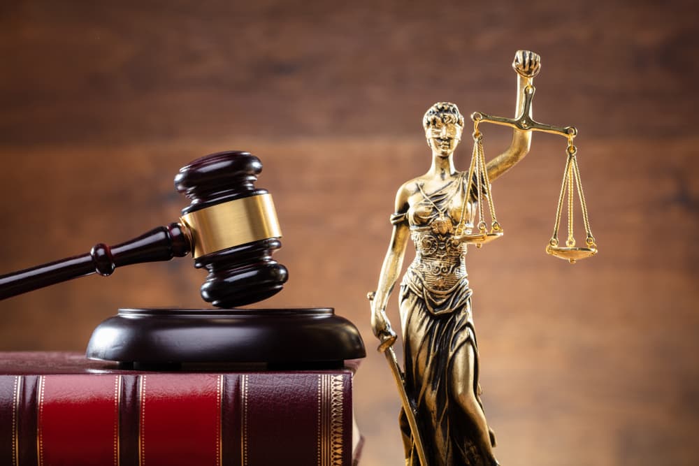 Close-up of a golden Lady Justice statue next to a wooden gavel on a law book.