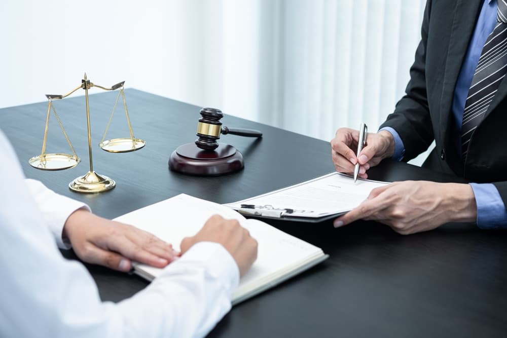 A professional male lawyer  discussing a legal case negotiation with a client in an office setting, reviewing a contract document related to law and justice.